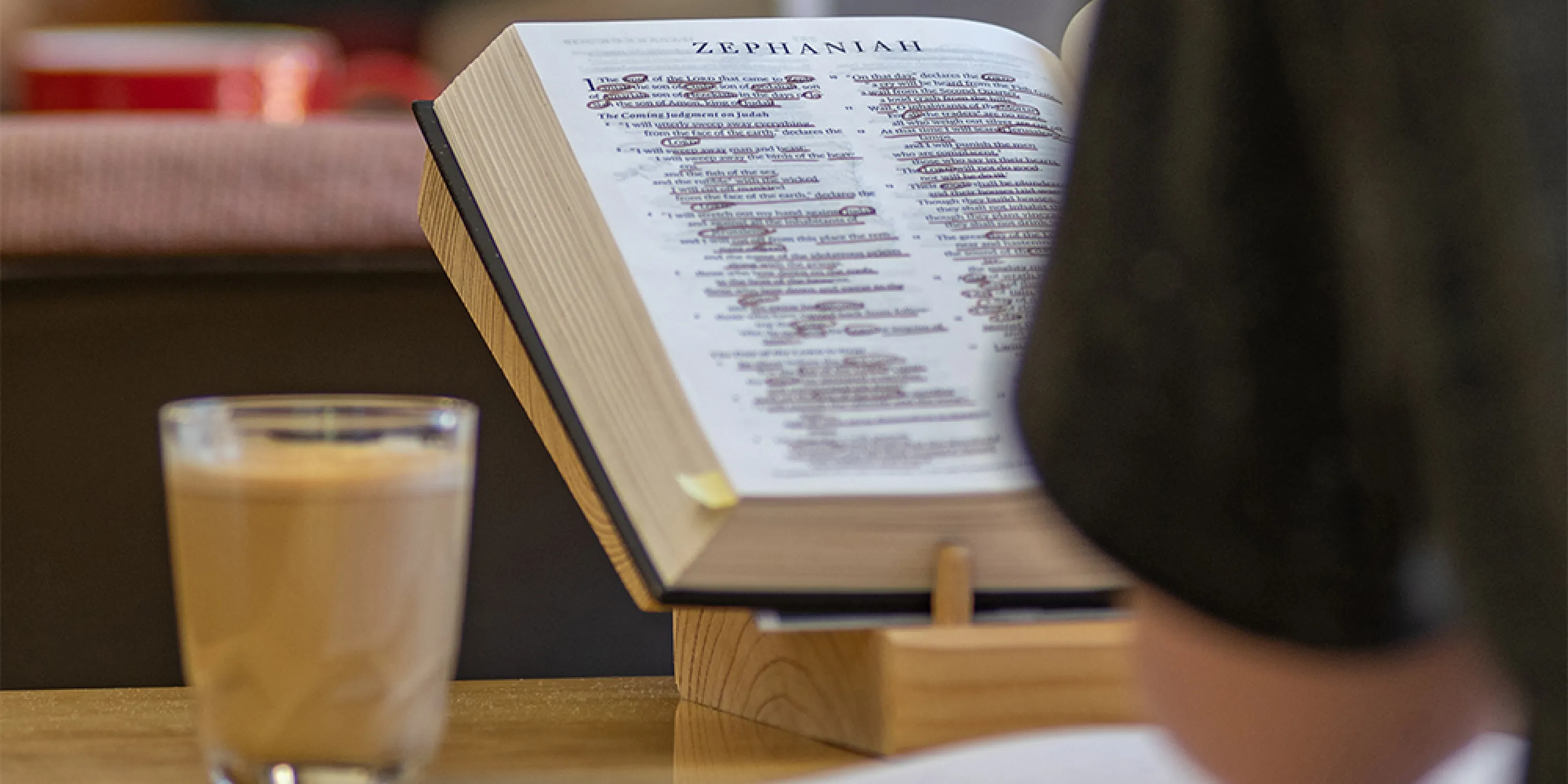 A close up image of a bible propped up on a desk next to a drink.