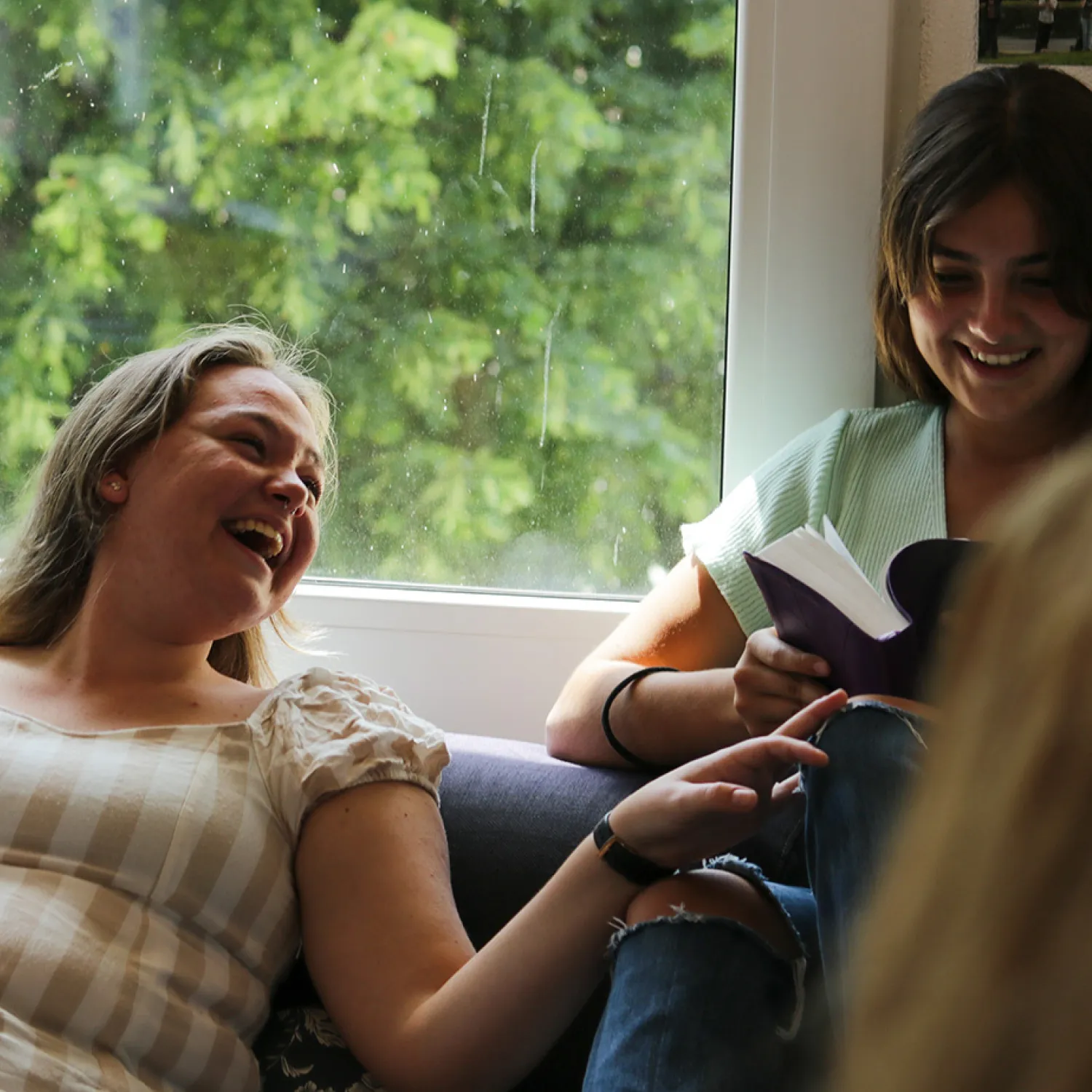 A couple of students on the couch reading the bible, laughing, and relaxing.