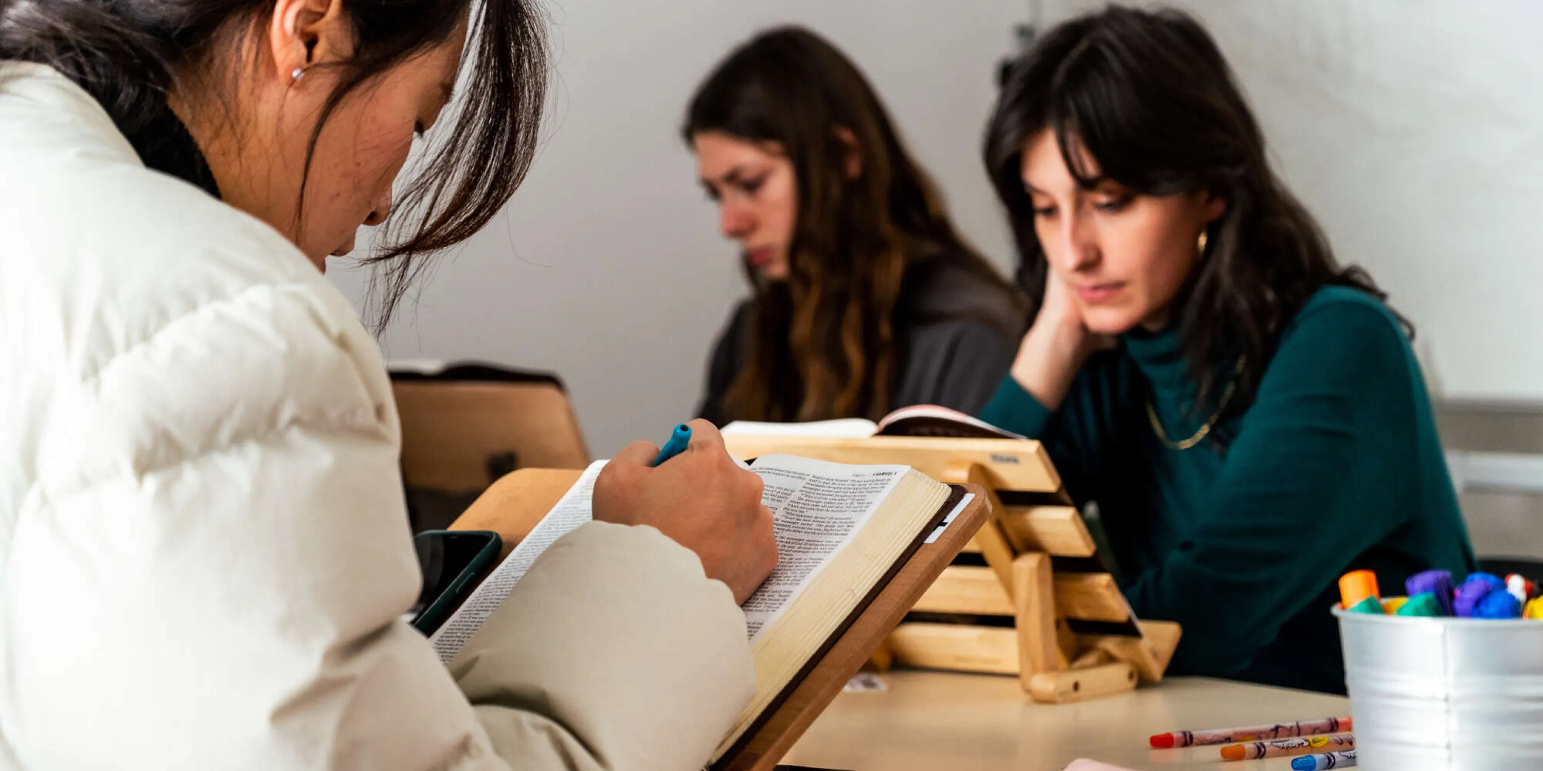 Three students studying their bibles at a desk.