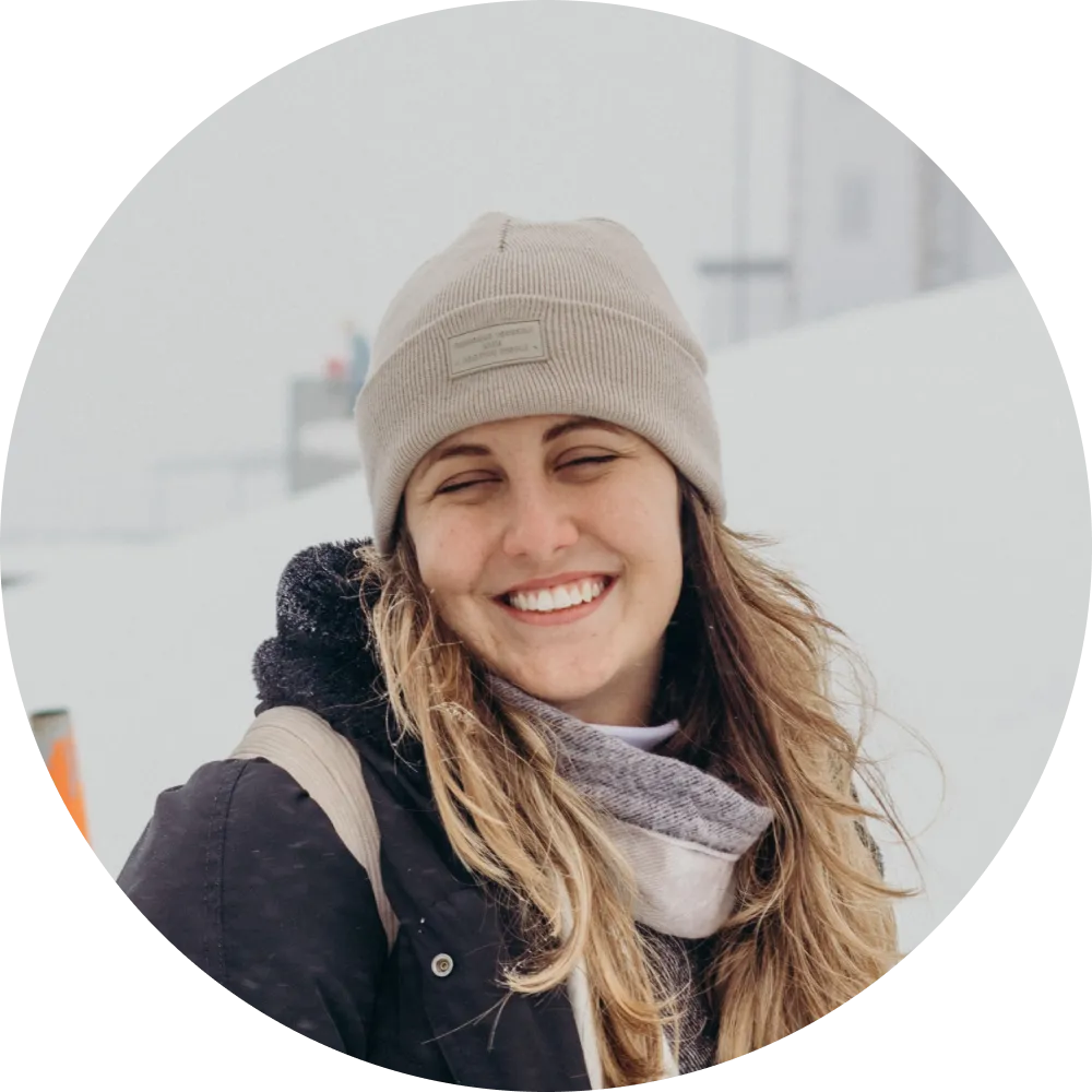 An image of a girl wearing a beanie in the snow and smiling at the camera.