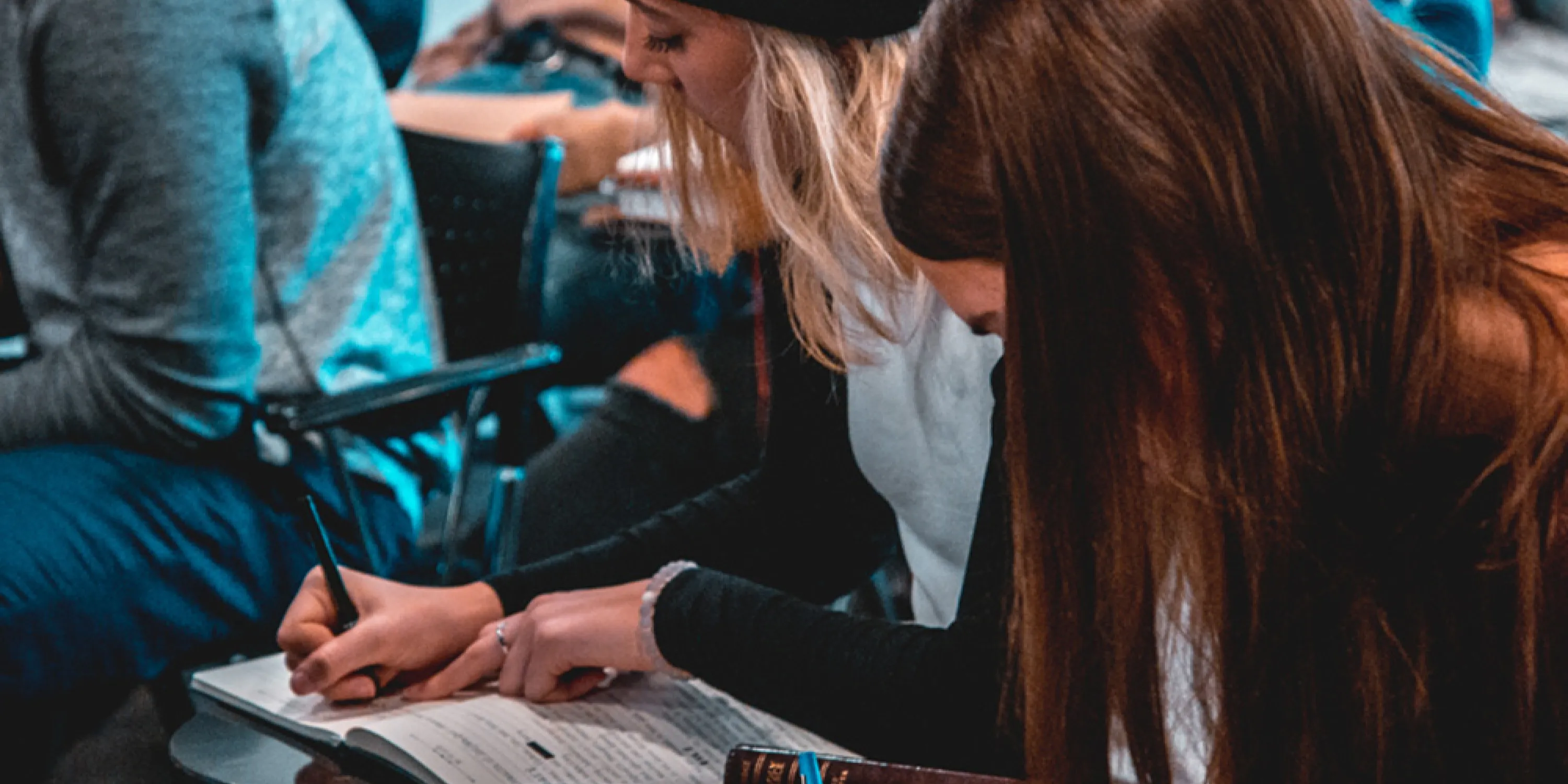 A couple of students seated and taking notes in a lecture room.