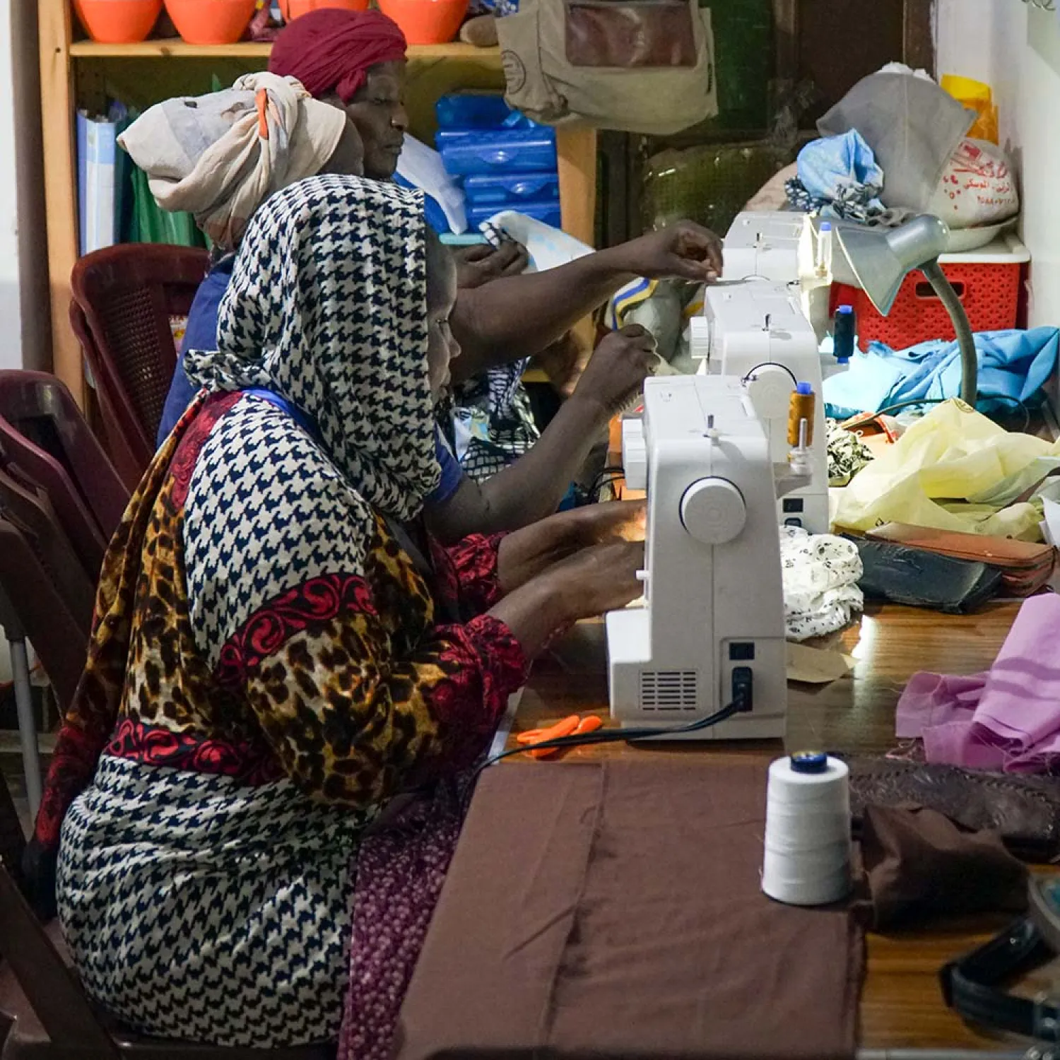 Women sitting at a table working at their sewing machines.