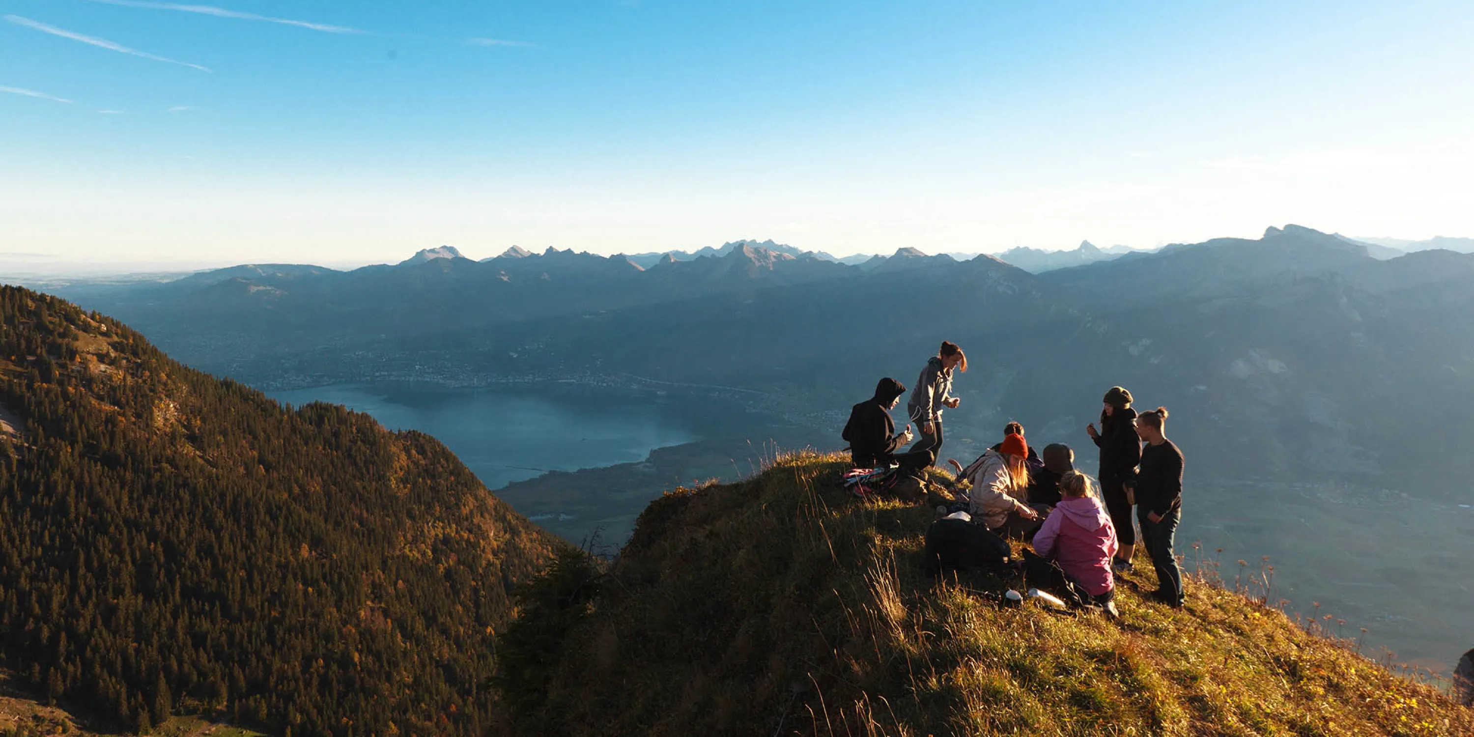 Students gathered at the top of a mountain overlooking a view of a lake.