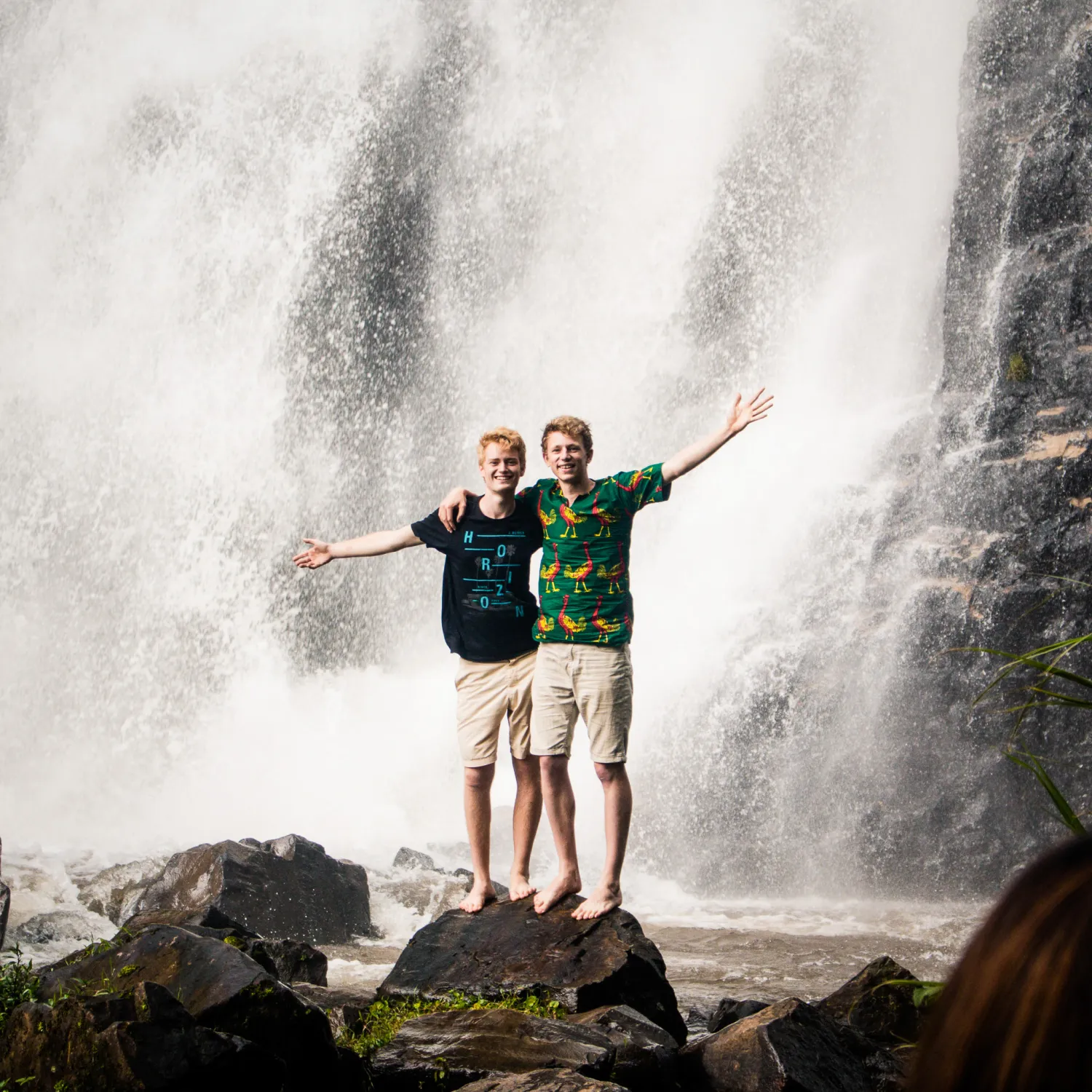 Two men front of a waterfall with their arms spread out during the DTS Outreach phase at YWAM Lausanne.
