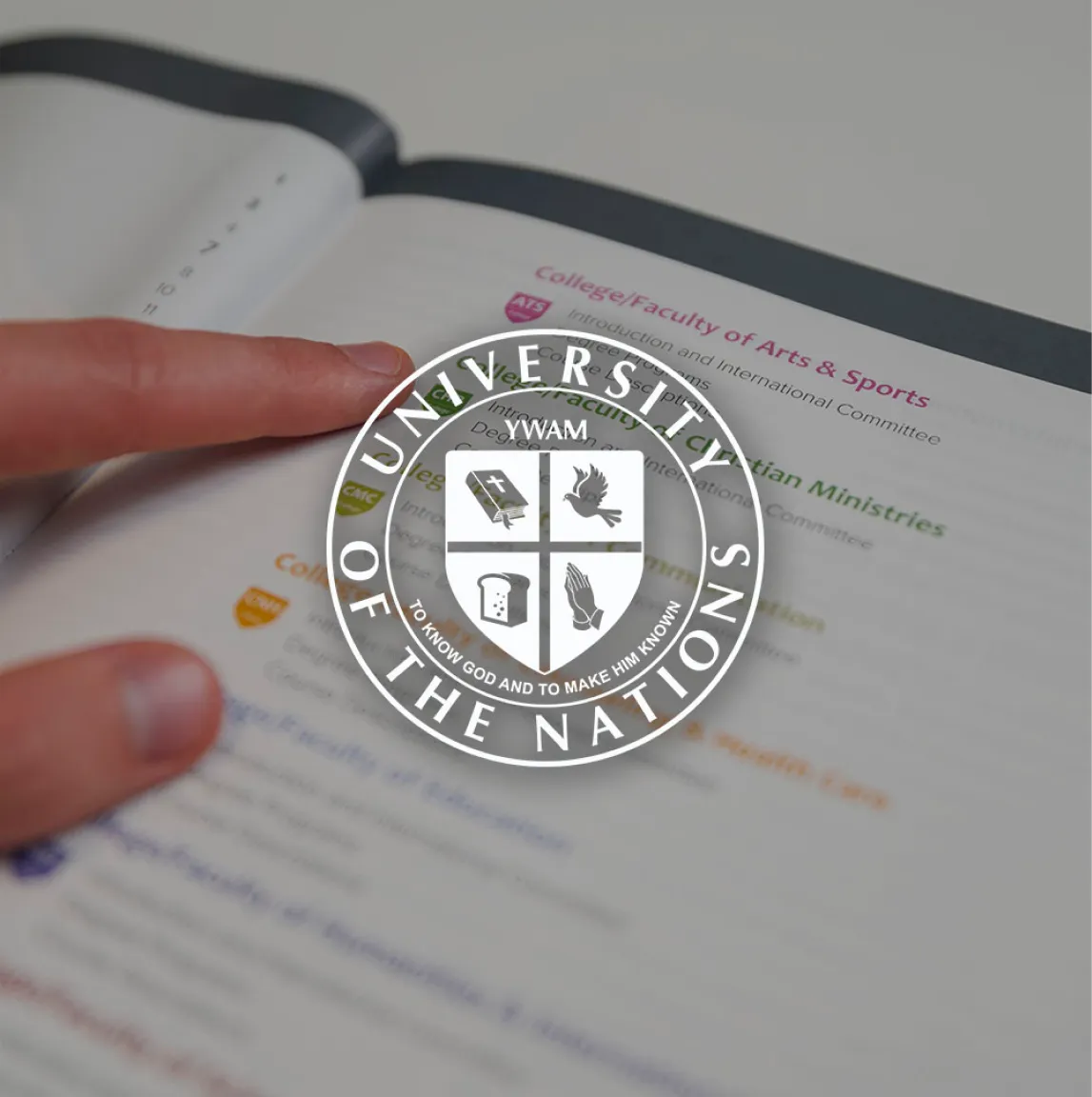 The University of the Nations logo overlaying a close up image of a hand pointing on text on a printed hand guide.