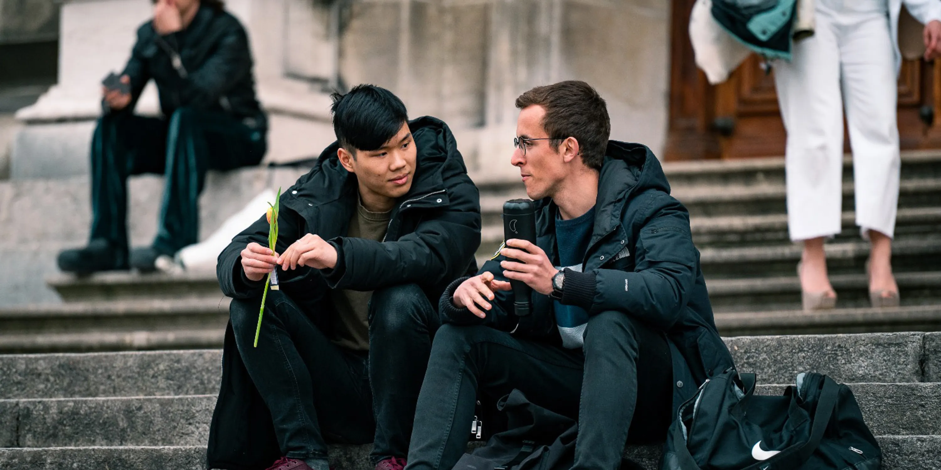 Two male students sitting on steps outside of a building.