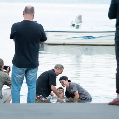 A couple of men baptising a third man in the water during the DTS Outreach phase at YWAM Lausanne.