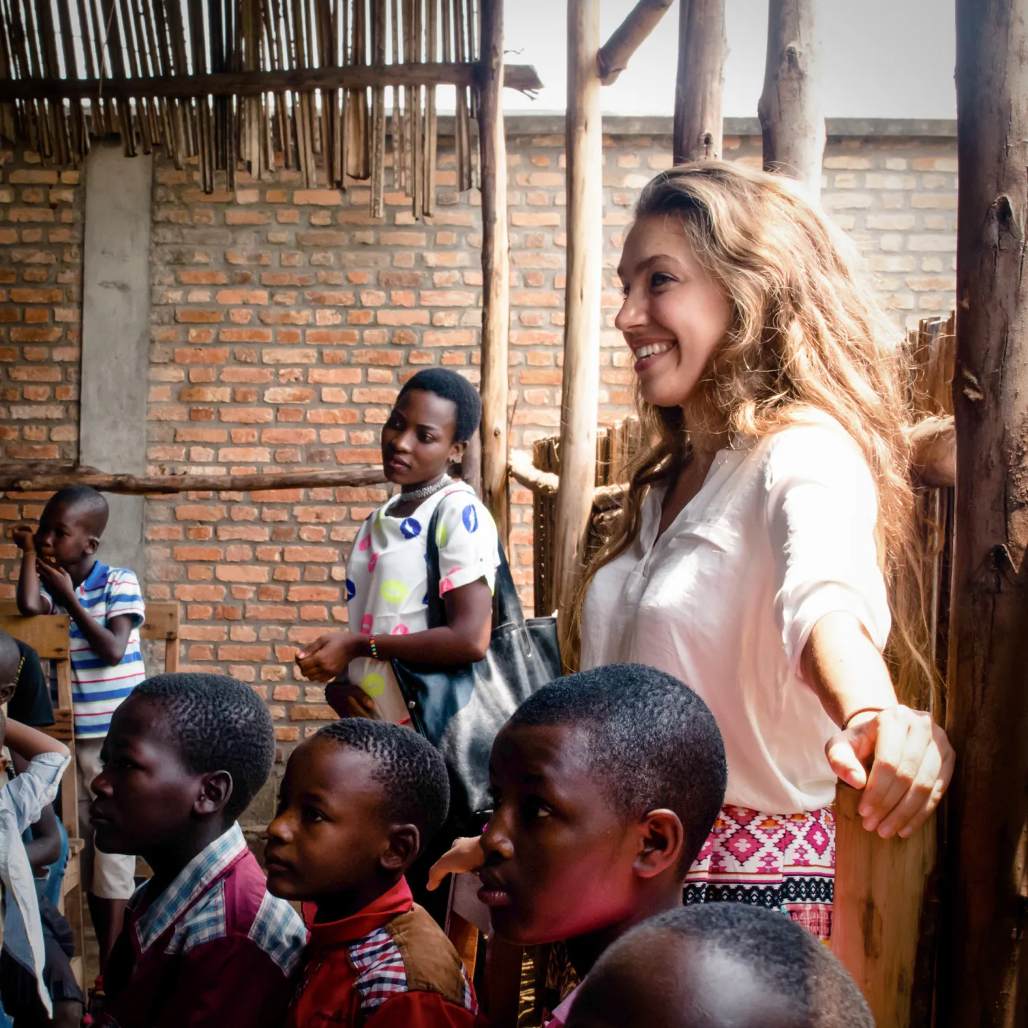 An outreach student standing smiling amongst a group of outreach children.