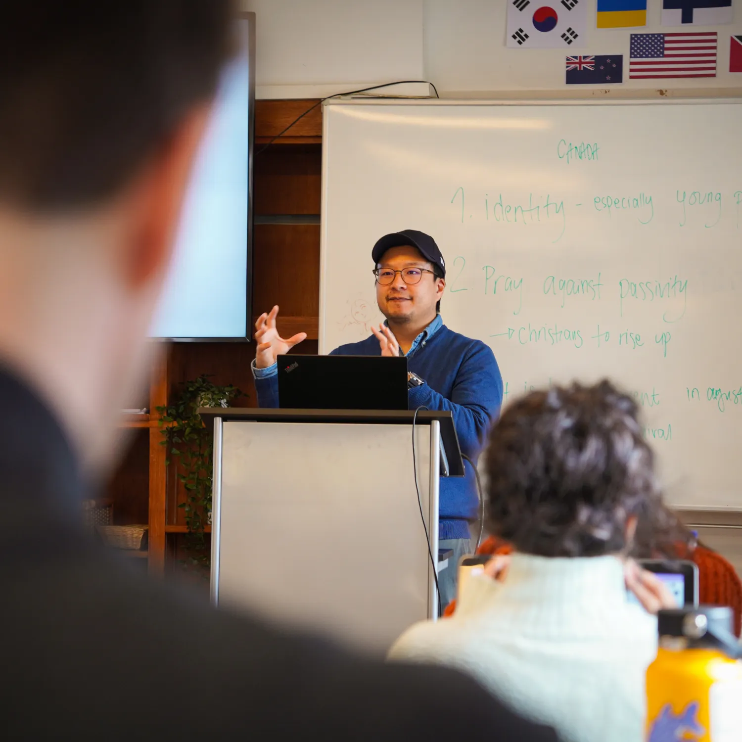 A lecturer teaching at a podium in front of a class of students.