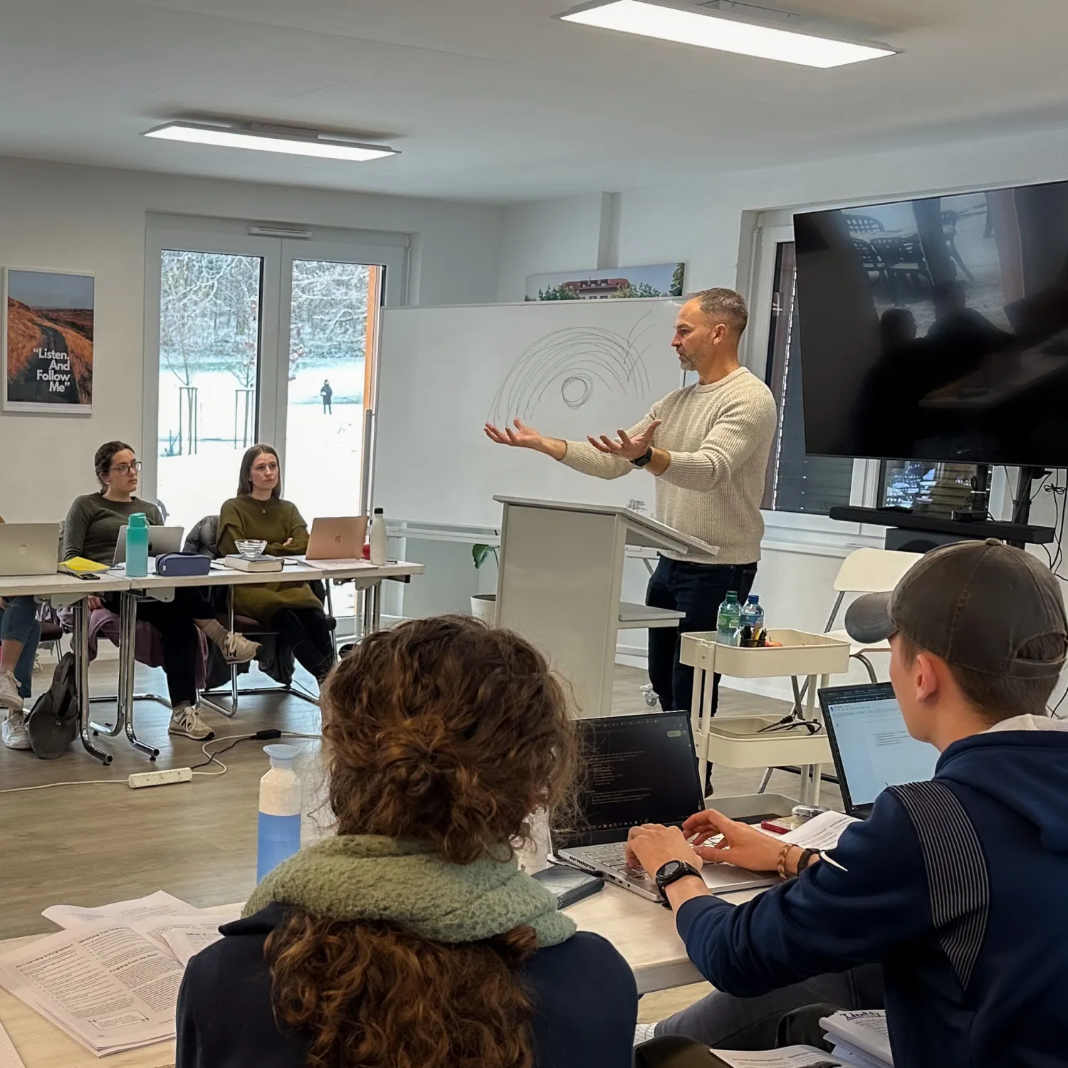 A lecturer standing in front of a group of seated students in a classroom.