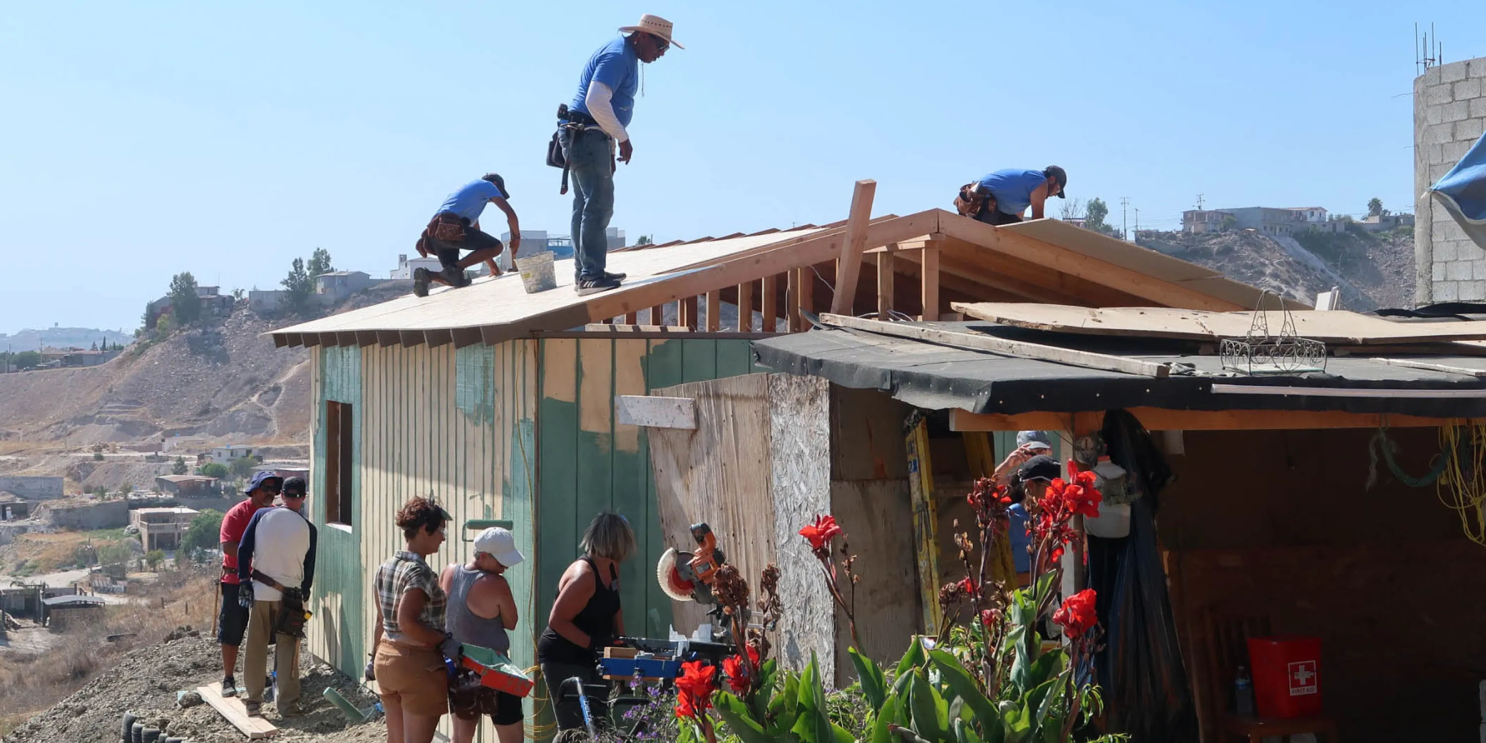 A group of adults working on the side and the roof a building outdoors.