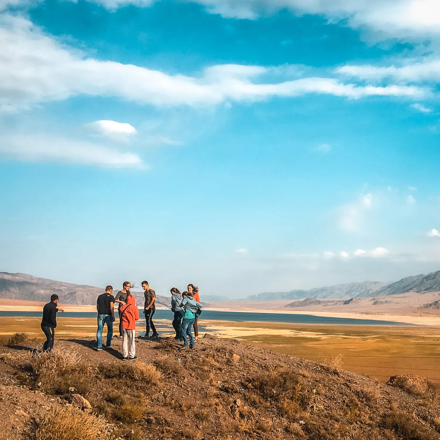 A group of students gathered on a plain of land with blue sky and mountains in the background.