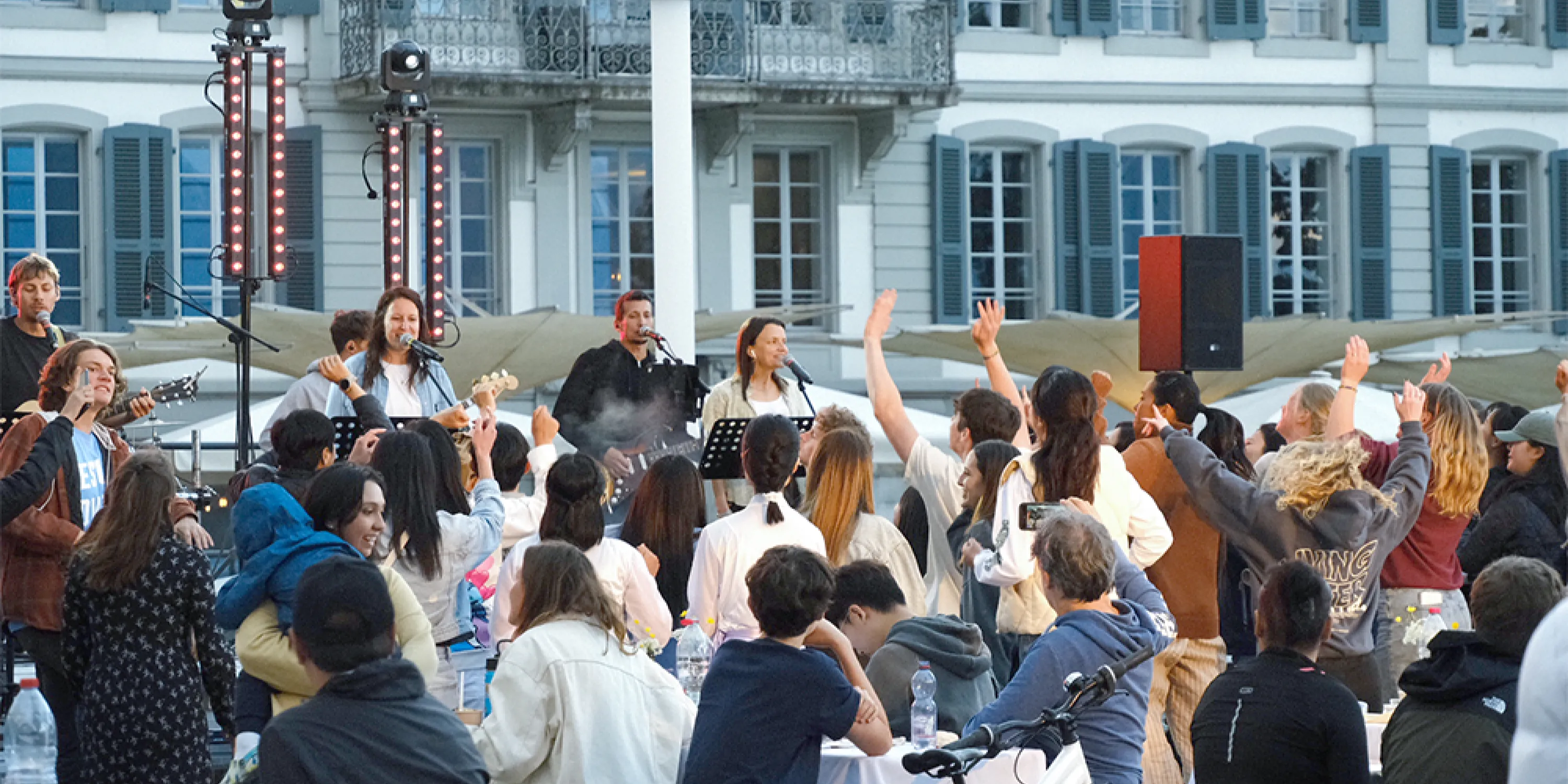 A crowd of students singing to performers on an outdoor stage.