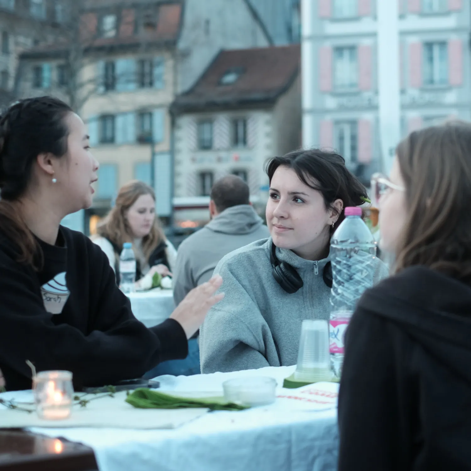 Students sitting outside at a table having a conversation with buildings in the background.