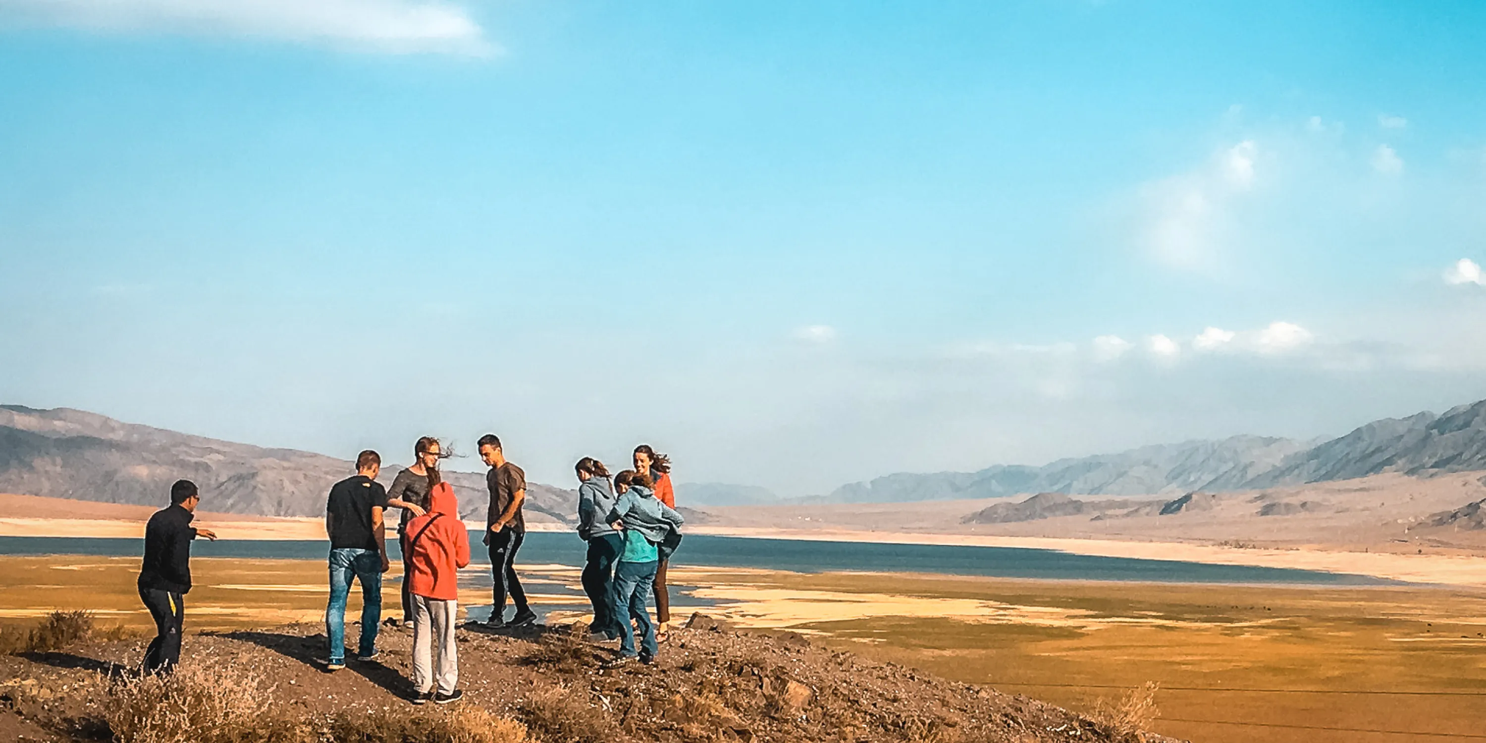 A group of students gathered on a plain of land with blue sky and mountains in the background.