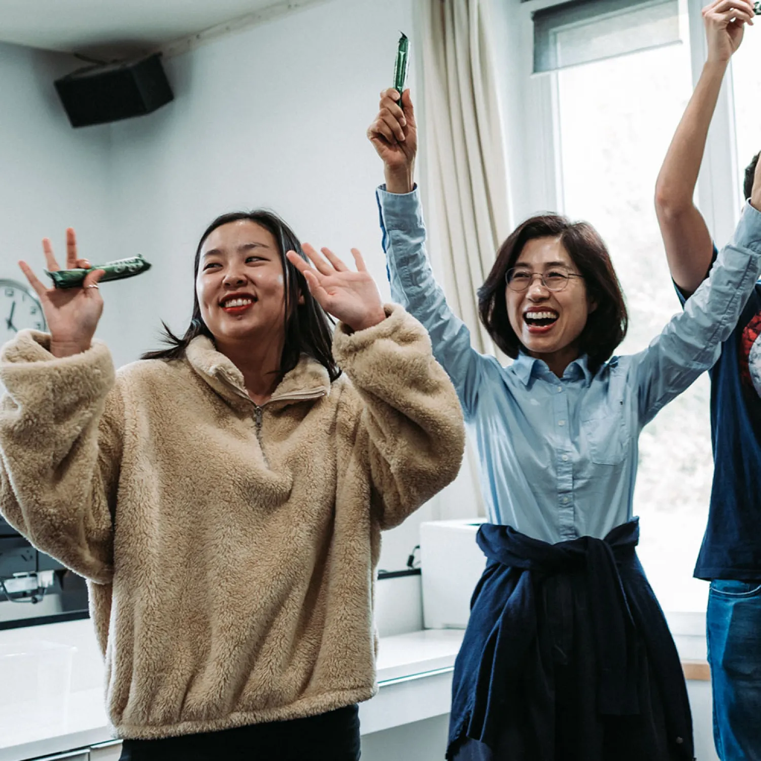 Two female students in a classroom smiling with their arms up in the air.