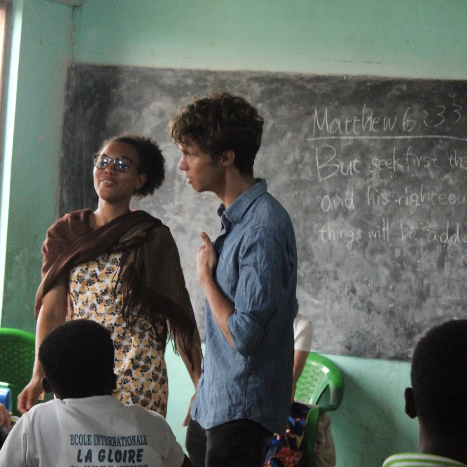 A teacher and a student engaging during a class in front of a chalk board 