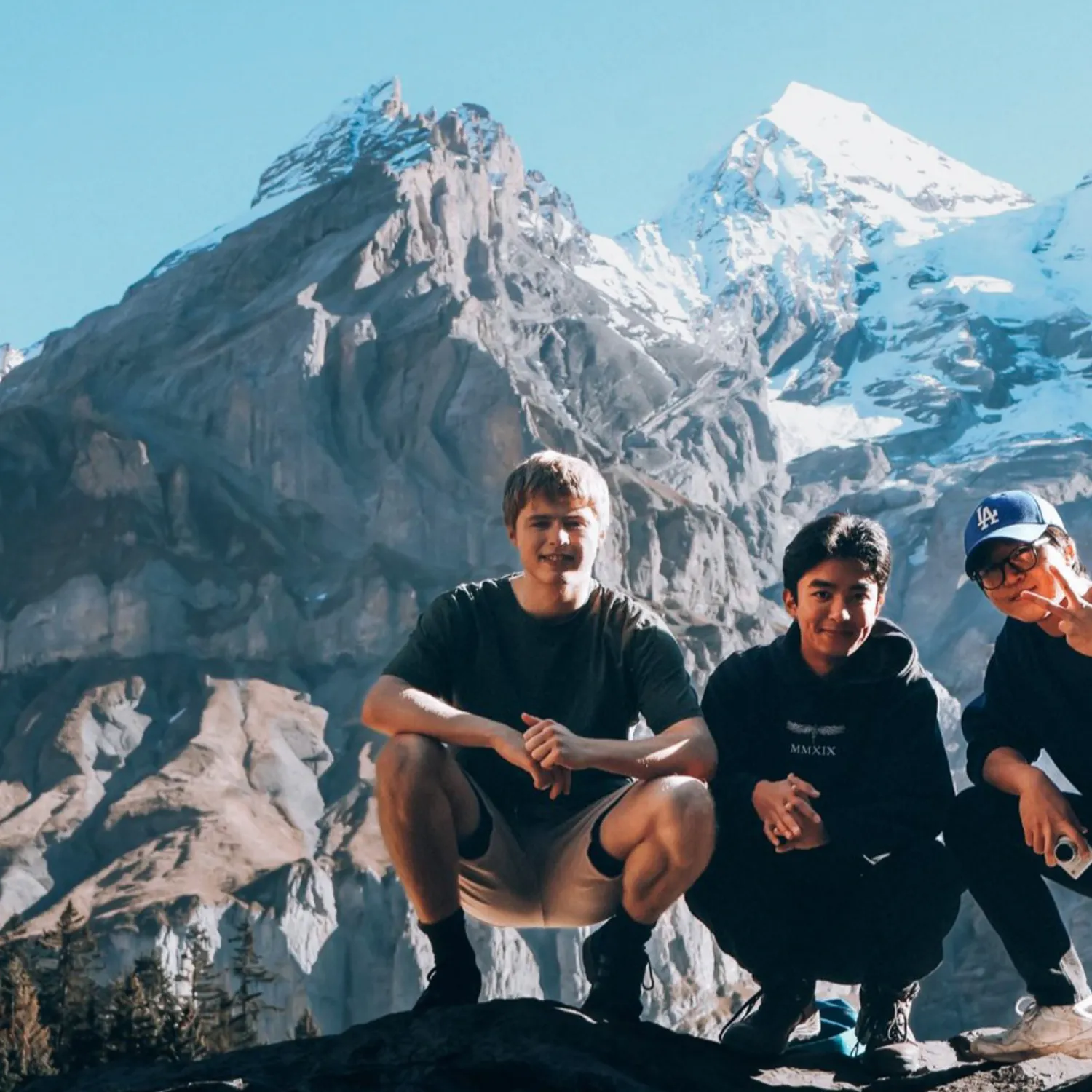 Three students crouched in front of a snowy mountain range.