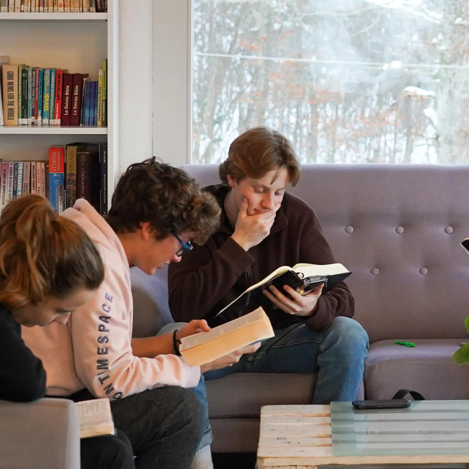 Three students sitting on a couch studying from books.