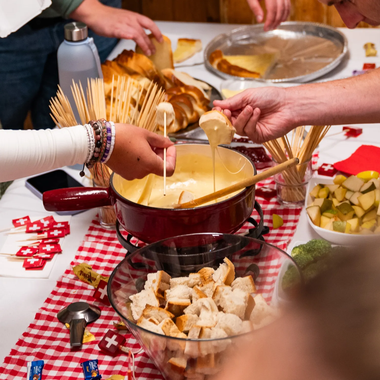A table spread containing Swiss dishes with hands reaching over dipping bread into fondue during DTS at YWAM Lausanne.