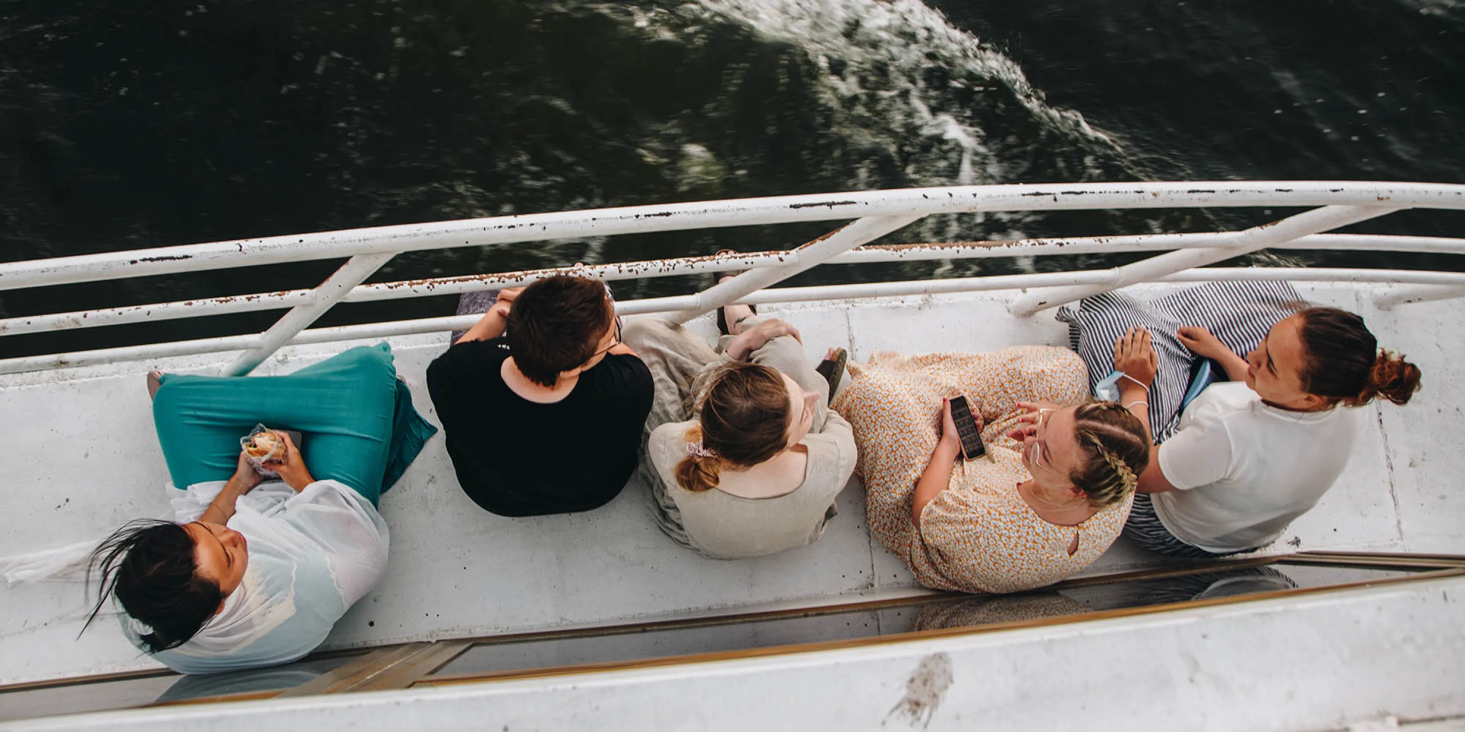 Overhead photo of students sitting on the side of a boat overlooking the sea.