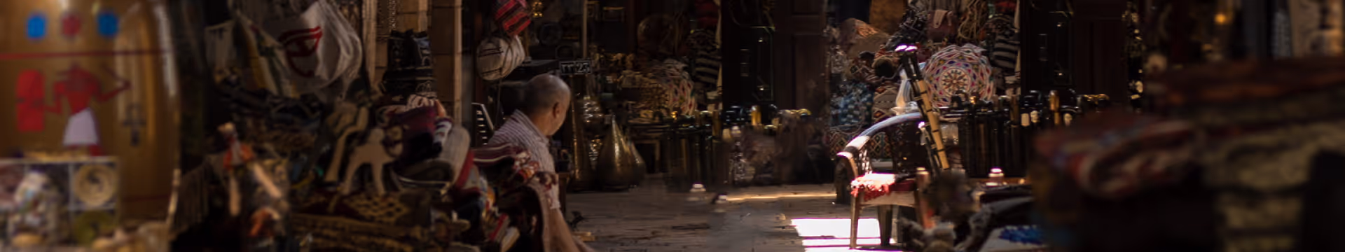 Inside a dimly lit market filled with various handcrafted goods and textiles, with a man sitting among the items.