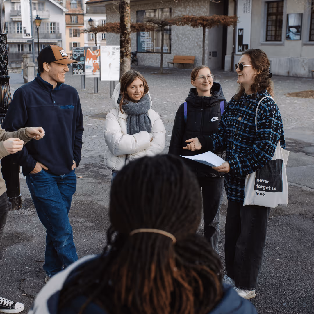 Group of young adults standing outside on a cobblestone street, smiling and conversing during a casual gathering.