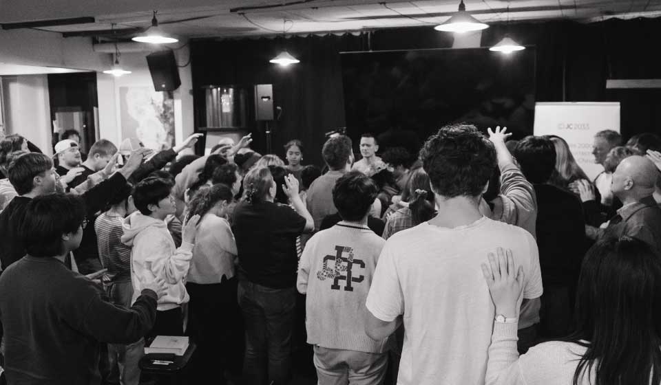 Group of people gathered indoors, some raising their hands, appearing engaged in an event or worship.